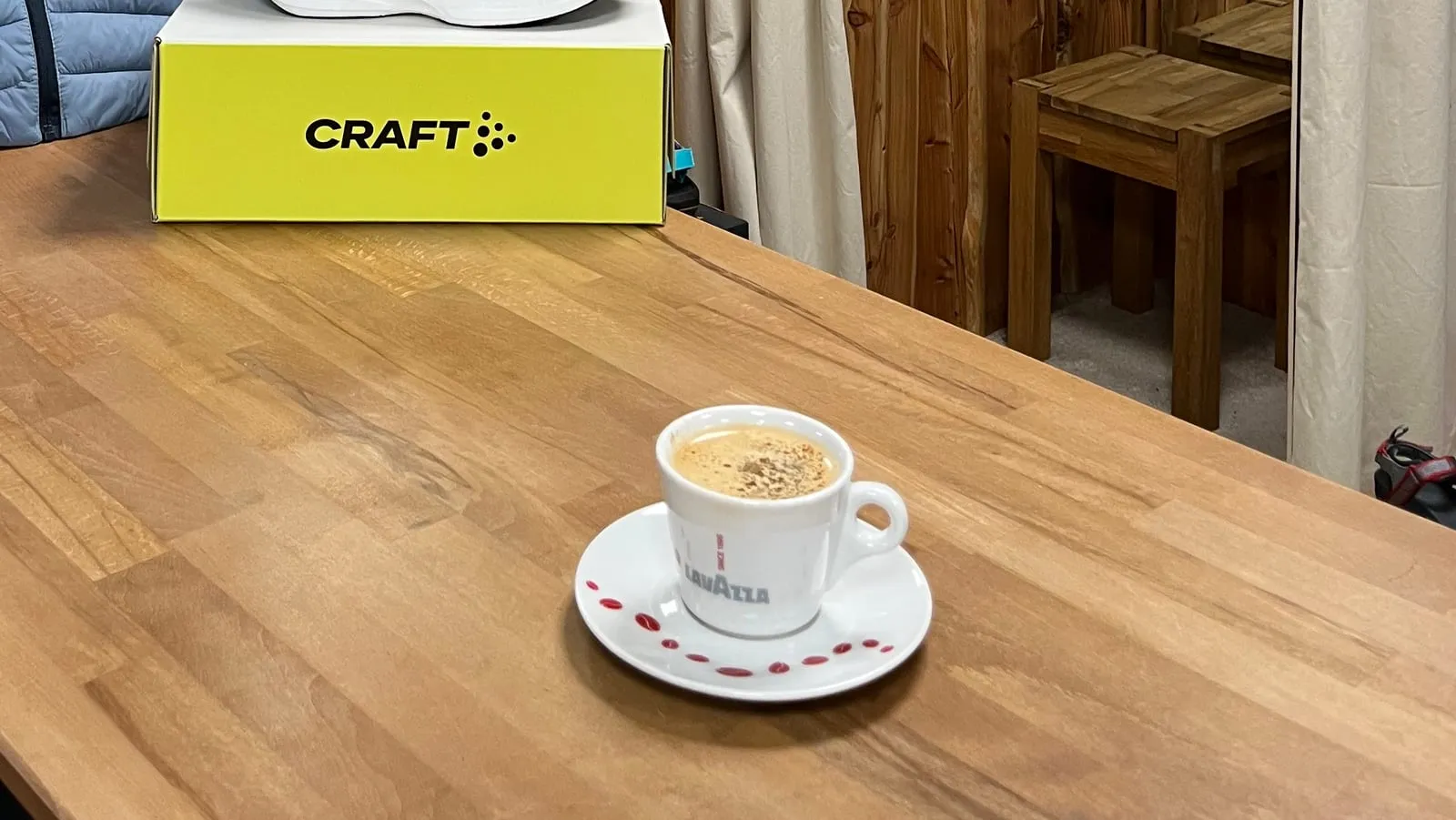 Tasse Kaffee auf der Holztheke neben einem Schuhkarton, dahinter die Umkleide